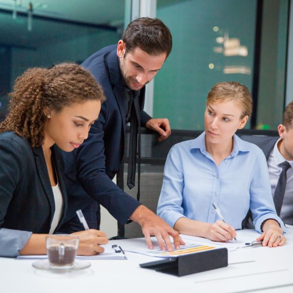 Business people sitting in conference room and discussing business issues. Executive manager standing, pointing to document and explaining his idea to business team